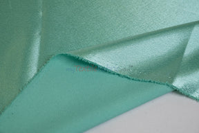 Seafoam-teal satin with a folded edge revealing the matte crepe-textured reverse