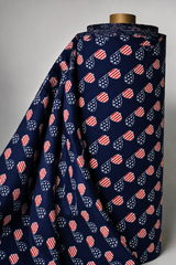 A roll of navy blue fabric draped over a wooden mannequin stand, featuring a repeating pattern of red and white striped heart-shaped sunglasses with white star details.