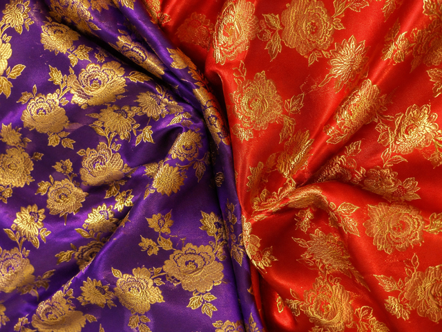 Purple and red brocade fabric with gold floral patterns, draped to show the texture and sheen.